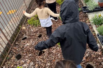 Bambini in fila nell'aiuola pronti a piantare le essenze floreali