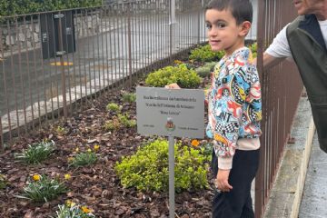 Bambino davanti a targa nell'aiuola con a fianco alpino